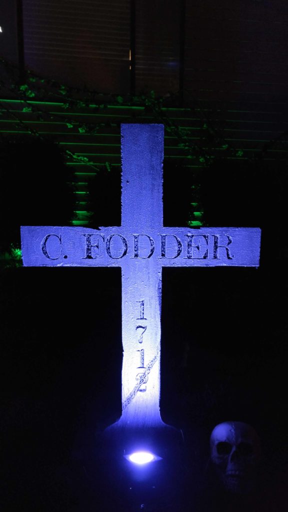 Cross shaped tombstone  with a epitaph that reads cannon fodder